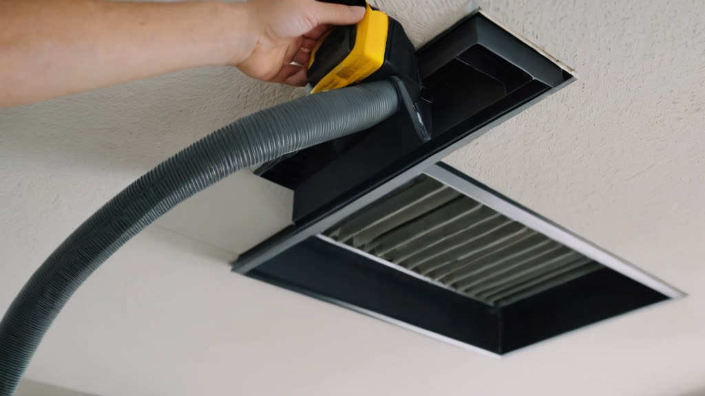 Cleaning dust from an HVAC vent with a vacuum attachment.